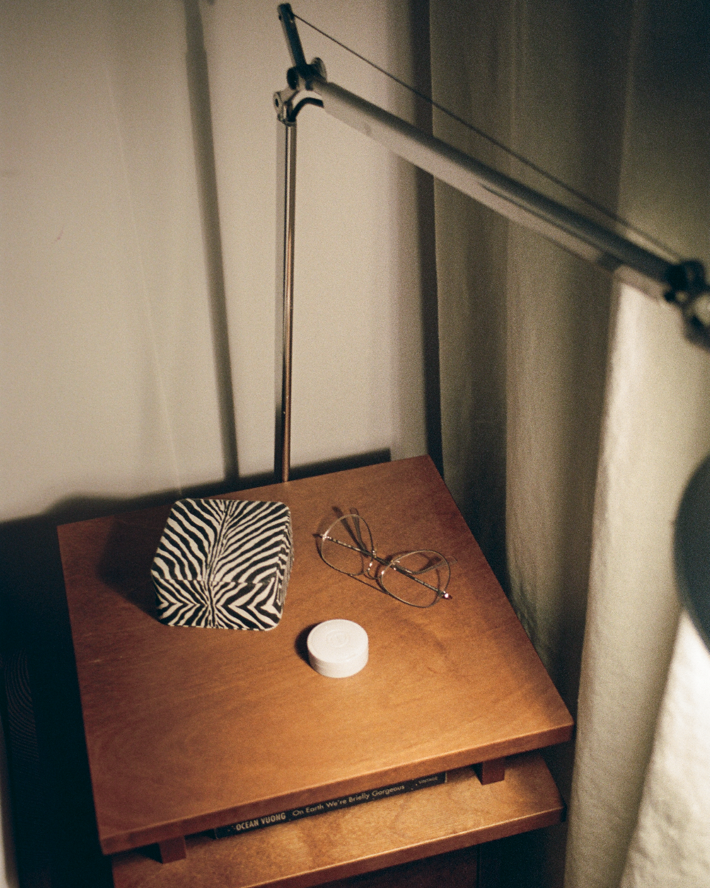 Wooden desk with zebra print object, glasses, and white container under a lamp in a dimly lit room.